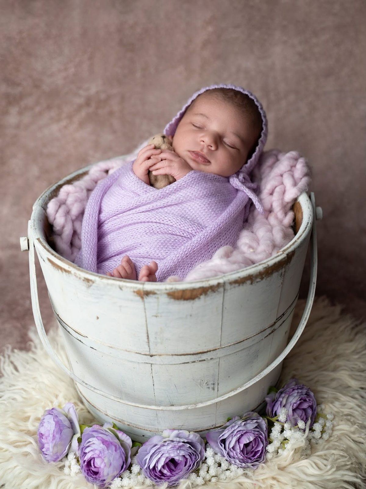 Newborn wrapped in lilac, nested in a painted bucket with roses