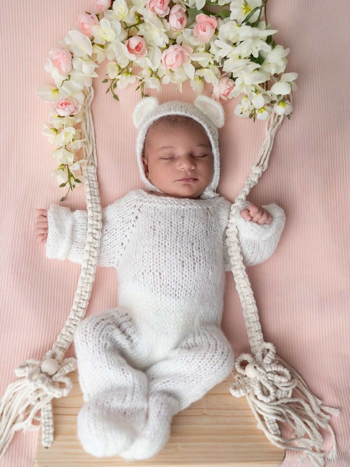 Newborn in a knit bear suit on a floral swing